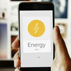 Mano sujetando un smartphone con una app de monitorización energética. El icono de un rayo y la palabra "Energy" indican el control del consumo.