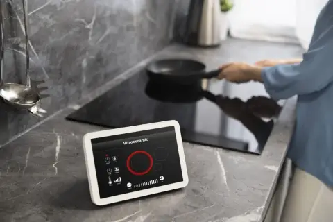 Cocina moderna con vitrocerámica y tablet para controlar electrodomésticos inteligentes. Una persona cocina en la placa de inducción.
