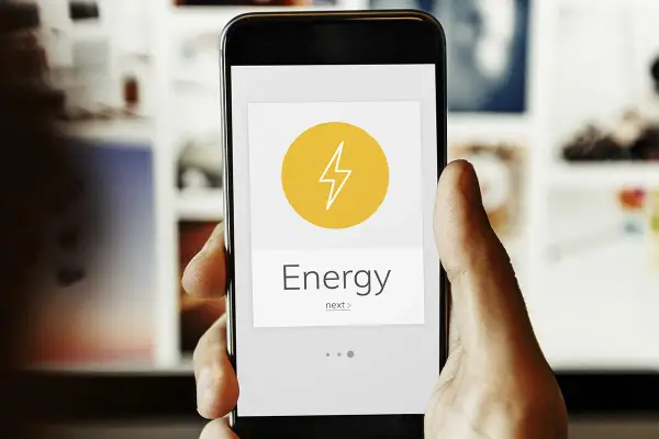 Mano sujetando un smartphone con una app de monitorización energética. El icono de un rayo y la palabra "Energy" indican el control del consumo.