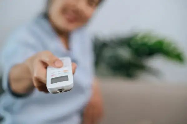 Persona sonriente ajusta el aire acondicionado con el mando. Controla la potencia aire acondicionado kw para un confort ideal.